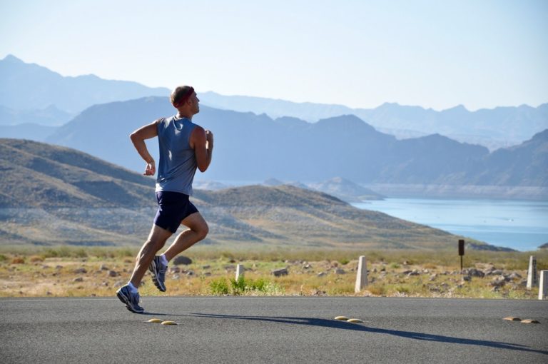 man running on the road through a mountain valley, next to a lake
